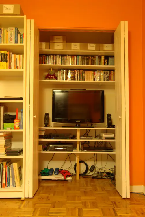 Opened cabinet doors showing a TV, game consoles, a DVD player, DVDs.